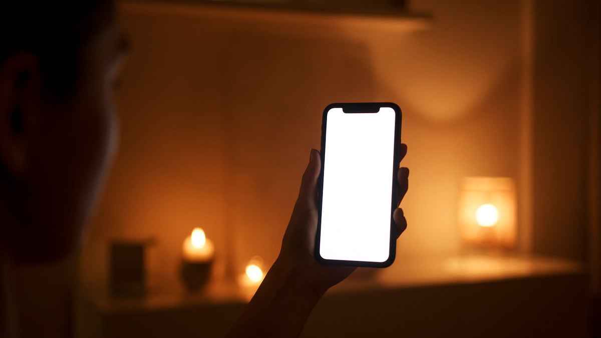 Человек в тёмной комнате держит смартфон, проверяет переписку, программа страха потери