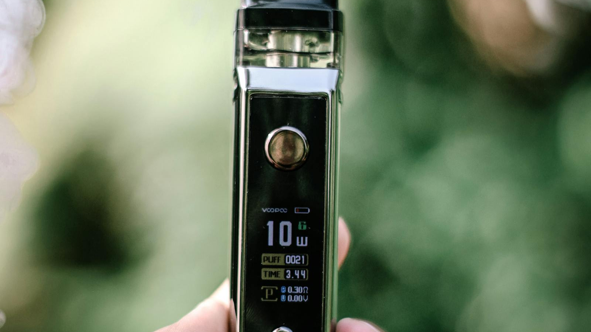 Vape-устройство с парами на тёмном фоне, размытый свет вечернего окна, рука держит pod-систему, атмосфера задумчивости
